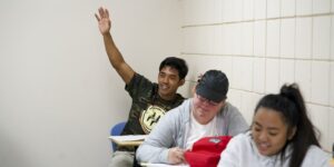 sociology student with hand raised in classroom at Chaminade
