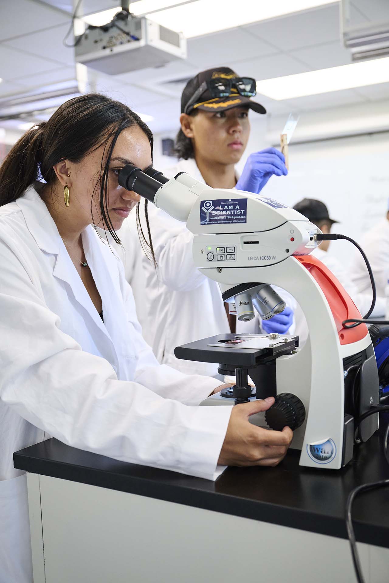 a student looking through the microscope while the other looks at a slide