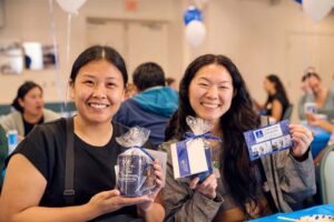 Ciena Alagao, MBA '23, left, and Carina Lee MEd '23 smile as they have their photo taken with their swag and photo booth image.