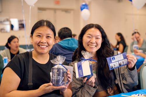 Ciena Alagao, MBA '23, left, and Carina Lee MEd '23 smile as they have their photo taken with their swag and photo booth image.